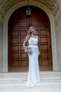 A woman in a white wedding dress standing on the steps of a building.