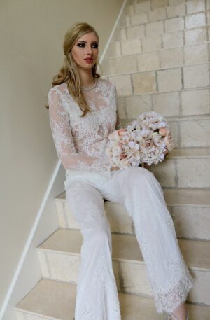 A beautiful woman in a white lace jumpsuit sitting on the stairs.