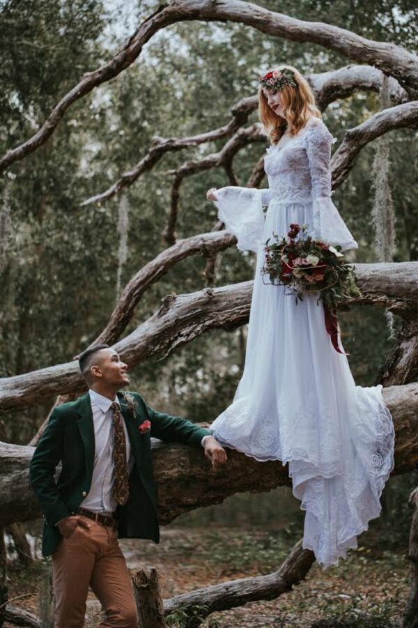 A bride and groom standing on a log in the woods, wearing the Fairy Tale wedding dress Juliett.
