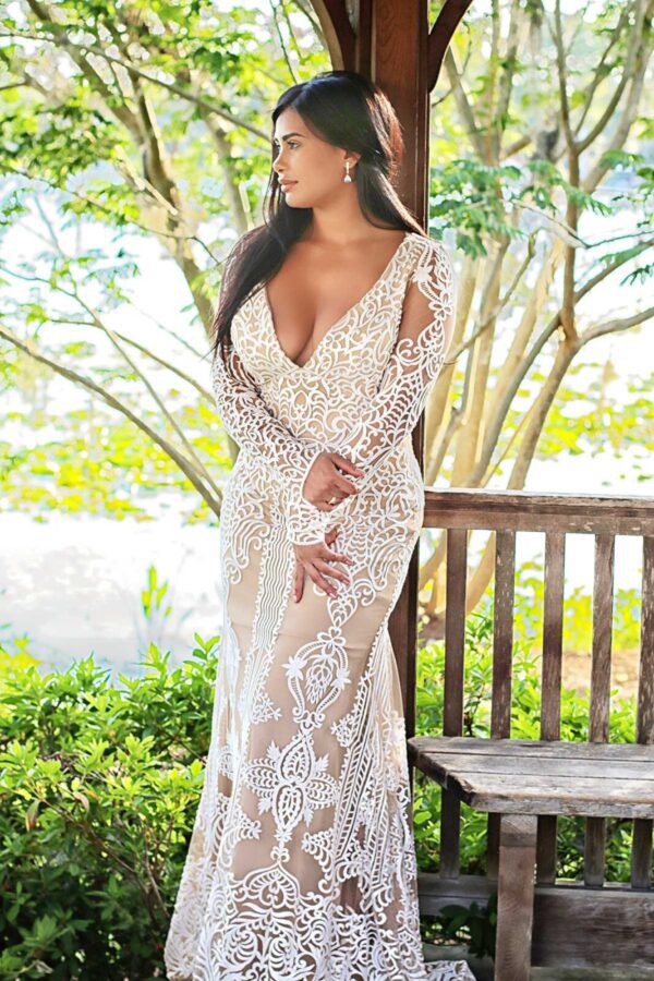 A woman in a white lace dress is posing on a wooden bench.