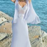 A woman in a white wedding dress is posing by the ocean.