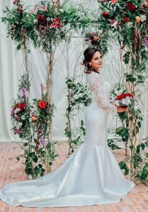 A bride in a white mermaid wedding dress posing in front of a floral arch.