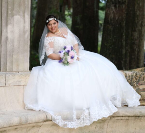 A bride in a wedding dress sitting on a stone bench.