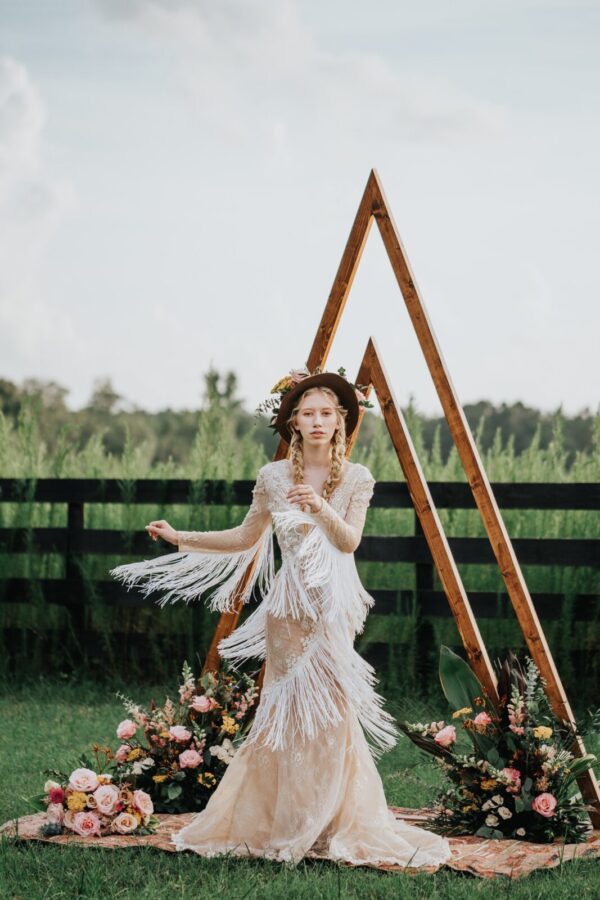 A bride in a bohemian wedding dress posing in front of a wooden triangle.