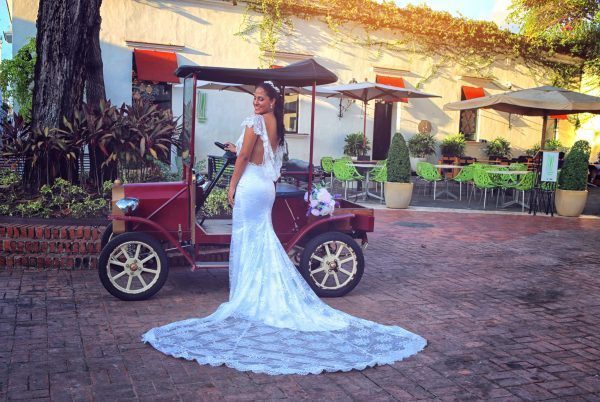 A bride in a wedding dress standing next to a vintage car.