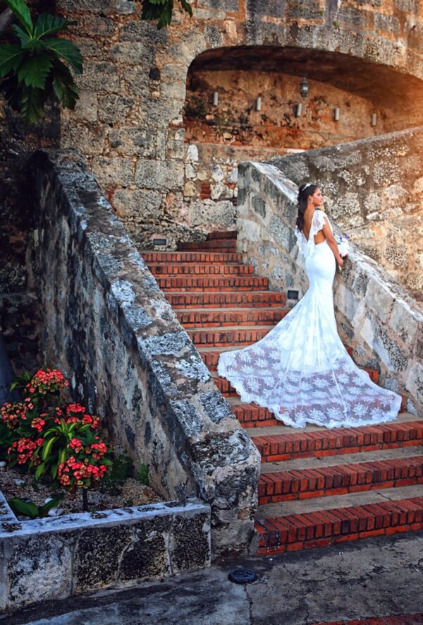 A bride in a lace wedding dress low back standing on a stone staircase.