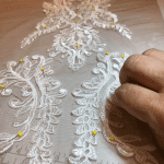A hand is delicately working on a white lace appliqué at a bridal shop.