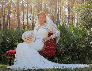 A bride in a lace dress sitting on a chair in the woods.