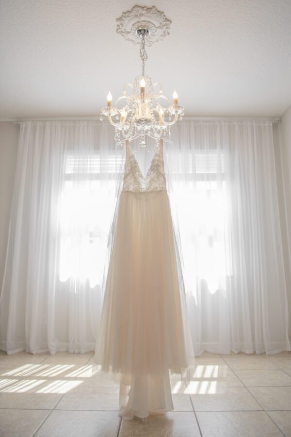 A Romantic Netting A-line Bridal Gown hangs on a chandelier in a room.