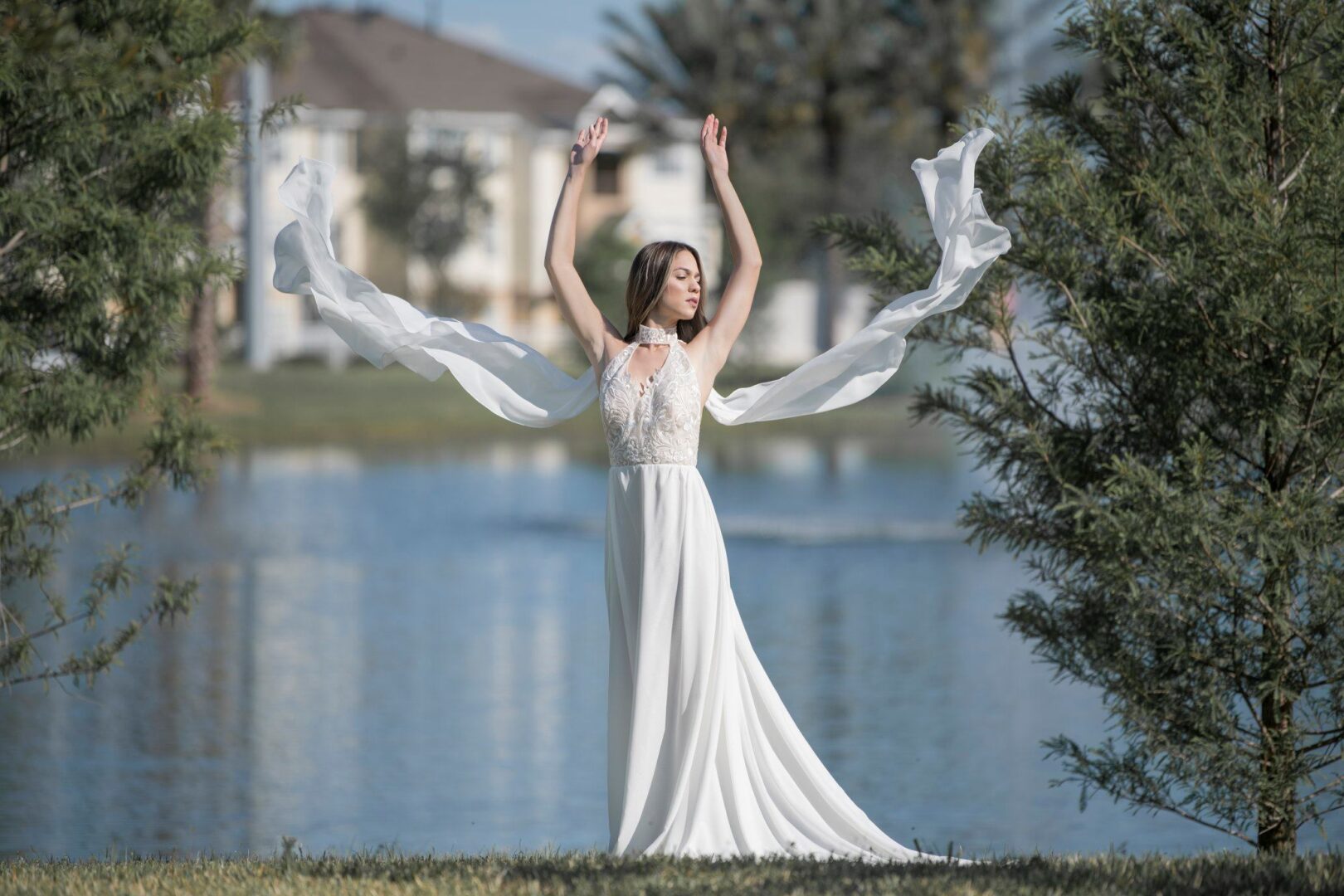 A bride in a Halter Top Chiffon Wedding Dress standing with her arms out in front of a lake.