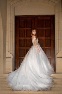 A couture bride, elegantly adorned in her wedding dress, stands on the steps of a church.
