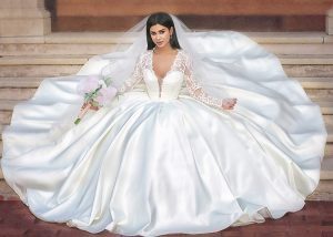 Bride seated with a big wide puffy Ivory wedding dress with a nice long cathedral veil holding a bridal bouquet, this beautiful long lace sleeves sating ball gown