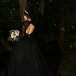 A bride in a black gown standing in the woods.