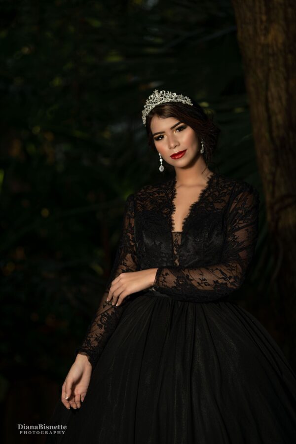 A woman in a black gown posing in the woods.