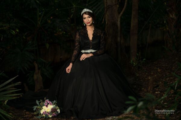 A bride in a black wedding dress posing in the woods.