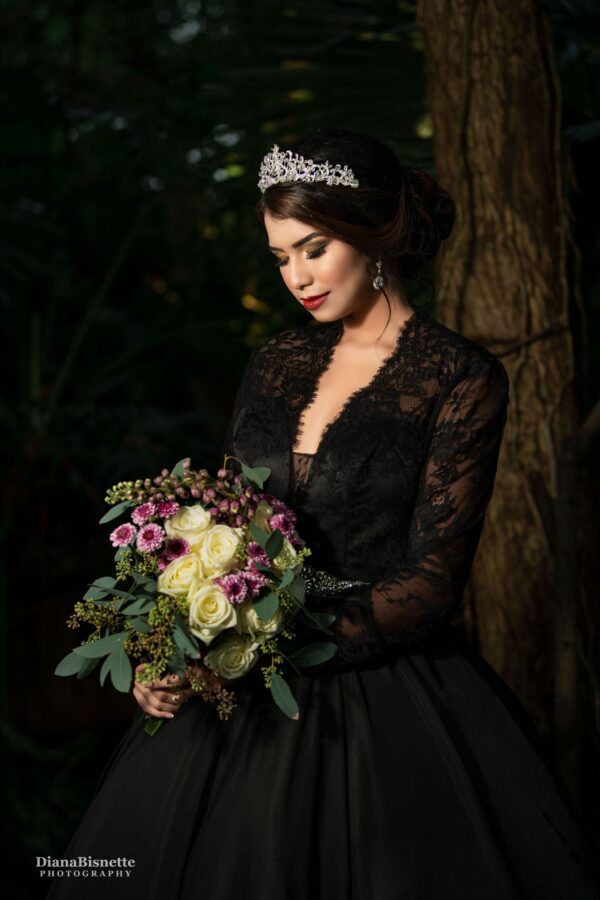 Bride wearing a long sleeve black lace wedding dress looking at her beautiful flowers