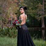 A bride in a black gown standing in a field with flowers for her bridal photoshoot in Florida.