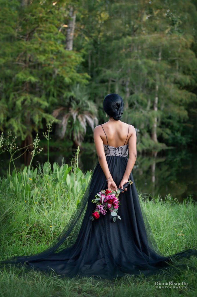 A bride looking at the lake showing the beautiful low back of her black wedding dress