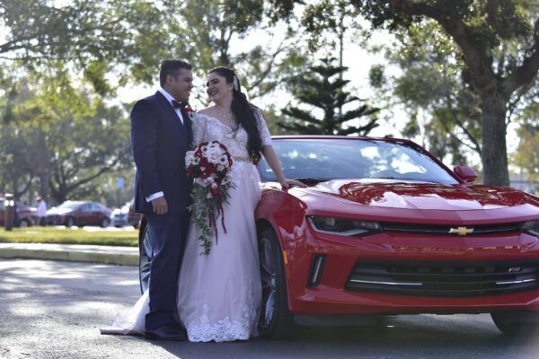 A Florida bride and groom standing next to a red Chevrolet Camaro.