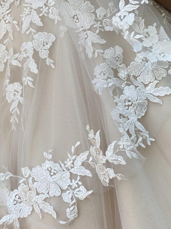 A close up of a wedding dress with lace and a handmade veil.