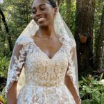 A woman in a wedding dress, wearing a handmade veil, smiling in the woods.
