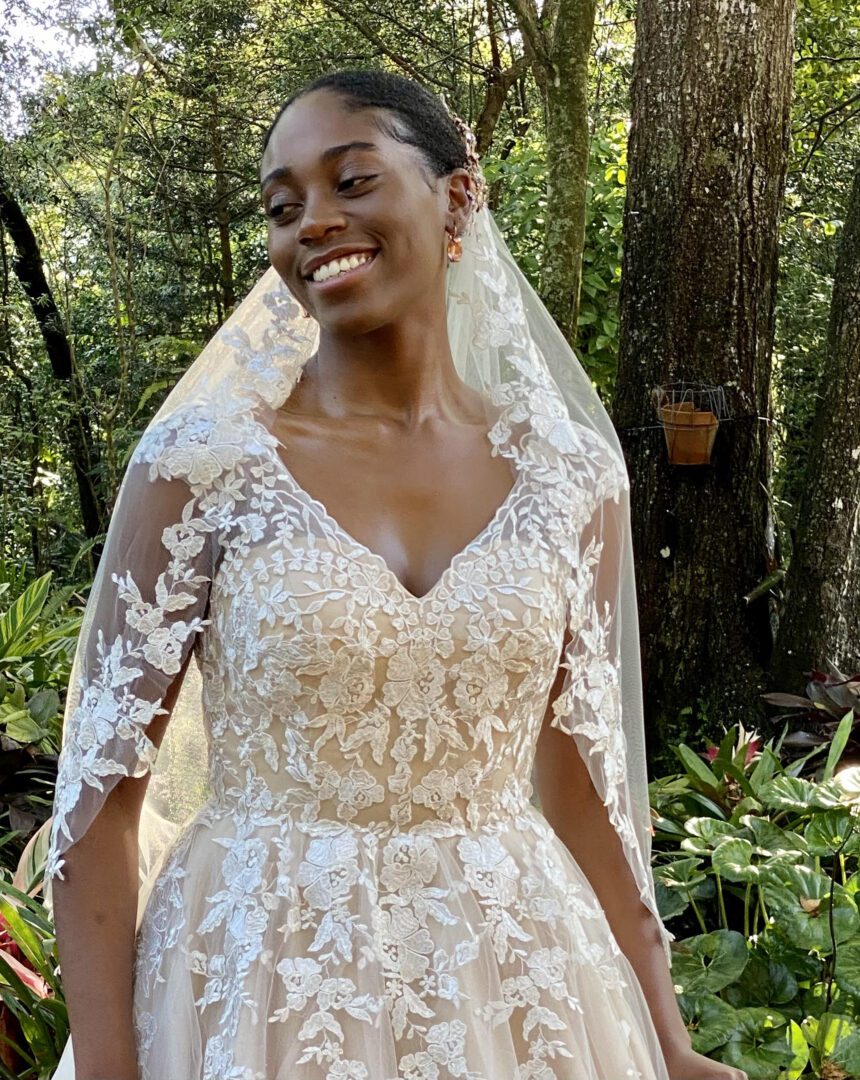 A woman in a wedding dress smiling in the woods.