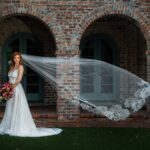 A Cathedral Wedding Veil bride posing with her wedding veil in front of a brick building.