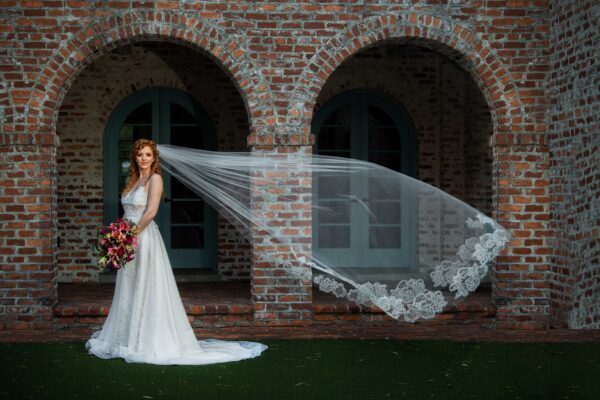 A Cathedral Wedding Veil bride posing with her wedding veil in front of a brick building.
