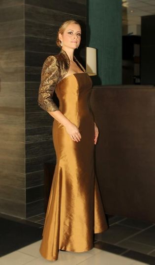 An elegant woman in a gold dress posing in a lobby.