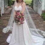 A red haired bride, designed by a wedding dress designer in Florida, holding a bouquet in front of an archway.