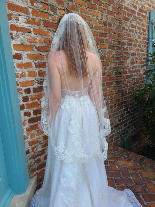 A woman wearing a Lace Bridal Veil V744 in front of a brick wall.