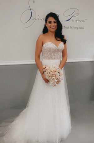A bride in a strapless wedding dress standing in front of a wall, showcasing her bridal elegance.