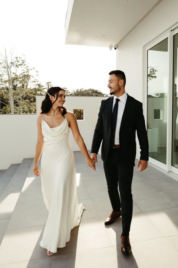 An elegant bride and groom strolling along the patio of a modern home, providing wedding dress inspiration.