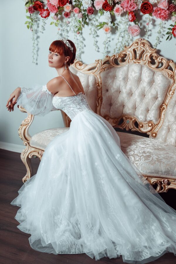 A beautiful woman in a wedding dress sitting on a couch while showing off the elegance of her bridal gown.