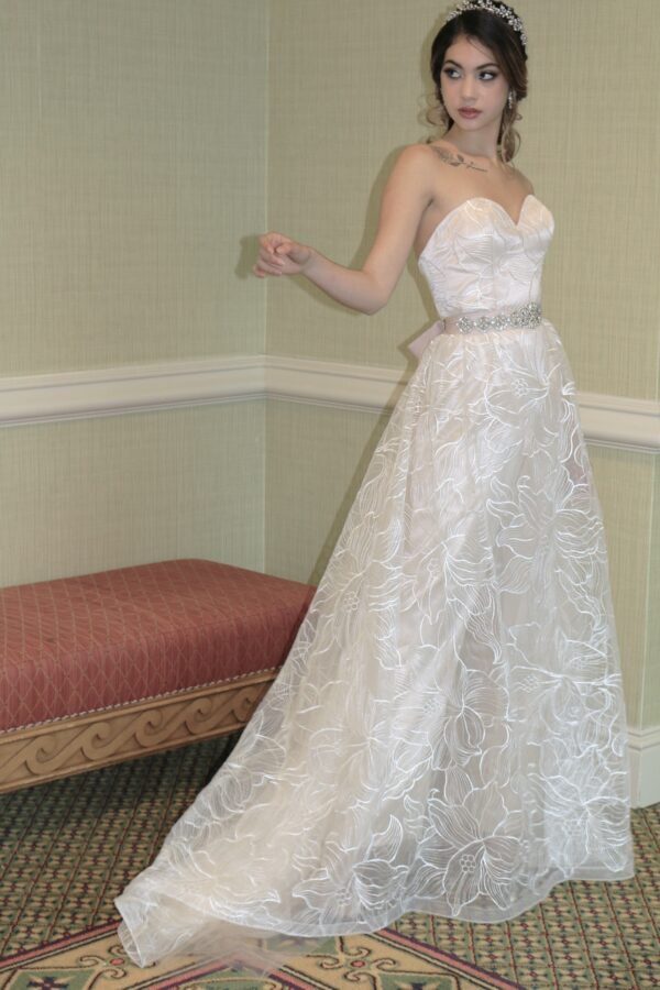 A woman in a white wedding dress posing in a room, showcasing the artistry of a Wedding Dress Designer.