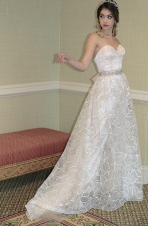A woman in a white wedding dress posing in a room, showcasing the artistry of a Wedding Dress Designer.