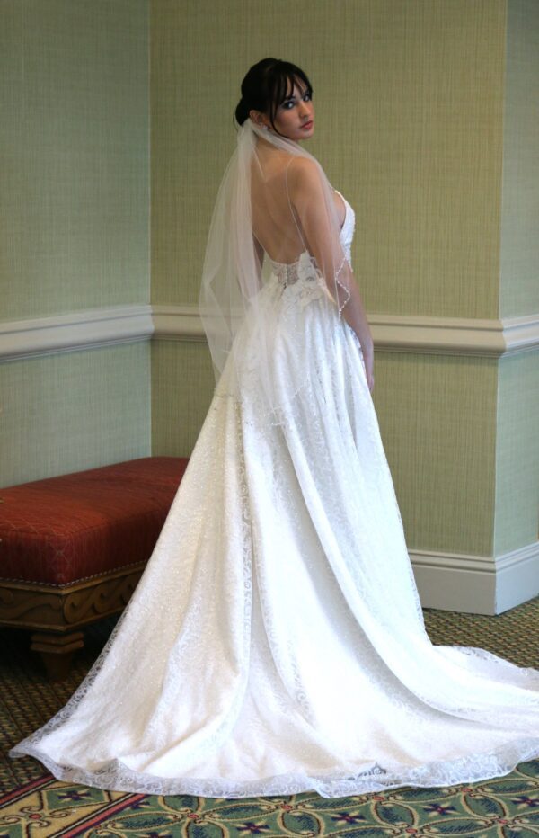 A bride in a stunning wedding dress, made to order by top wedding dress designers, poses elegantly in a room of the exquisite wedding dress shop in Orlando.
