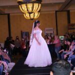 A bride in a wedding dress gracefully struts down the runway at a Bridal Fashion show.