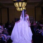 A woman in a bridal gown walks down the runway at a fashion show dedicated to wedding dresses.