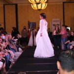 A woman is strutting down the runway in a captivating bridal gown at a glamorous bridal fashion show.