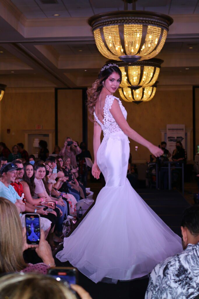 A woman in a white dress gracefully struts down the runway, showcasing the latest bridal fashion.