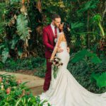 A bride and groom sharing a passionate kiss in a romantic tropical garden, providing wedding dress inspiration.