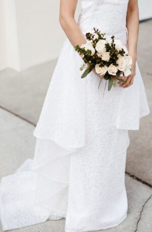 A bride in a white Sheath Sparkle wedding dress holding a bouquet, wearing a lace sheath wedding dress.
